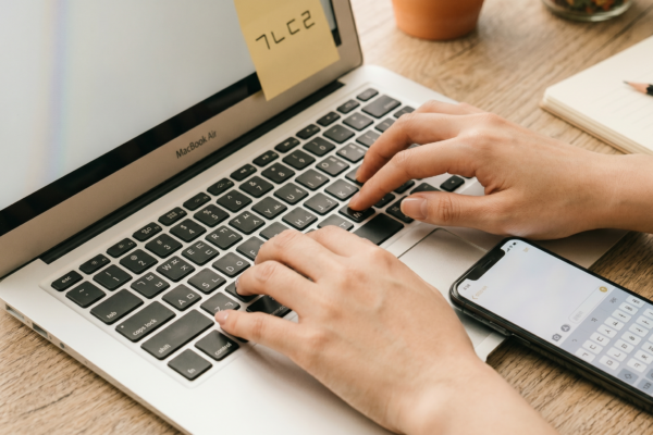 Hands typing on a MacBook with Korean Hangul keyboard, phone showing Korean keyboard beside it on wooden desk