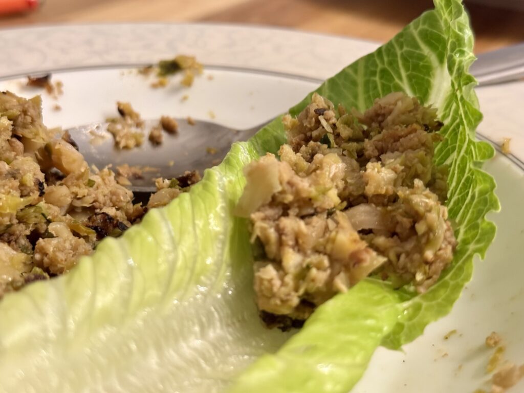 Smoky leftover cutlet filling spooned into a fresh lettuce leaf on a plate — Korean ssam-style lettuce wraps with chopped cutlets, caramelized onion, brussels sprouts, and zucchini.