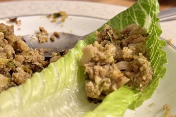 Smoky leftover cutlet filling spooned into a fresh lettuce leaf on a plate — Korean ssam-style lettuce wraps with chopped cutlets, caramelized onion, brussels sprouts, and zucchini.